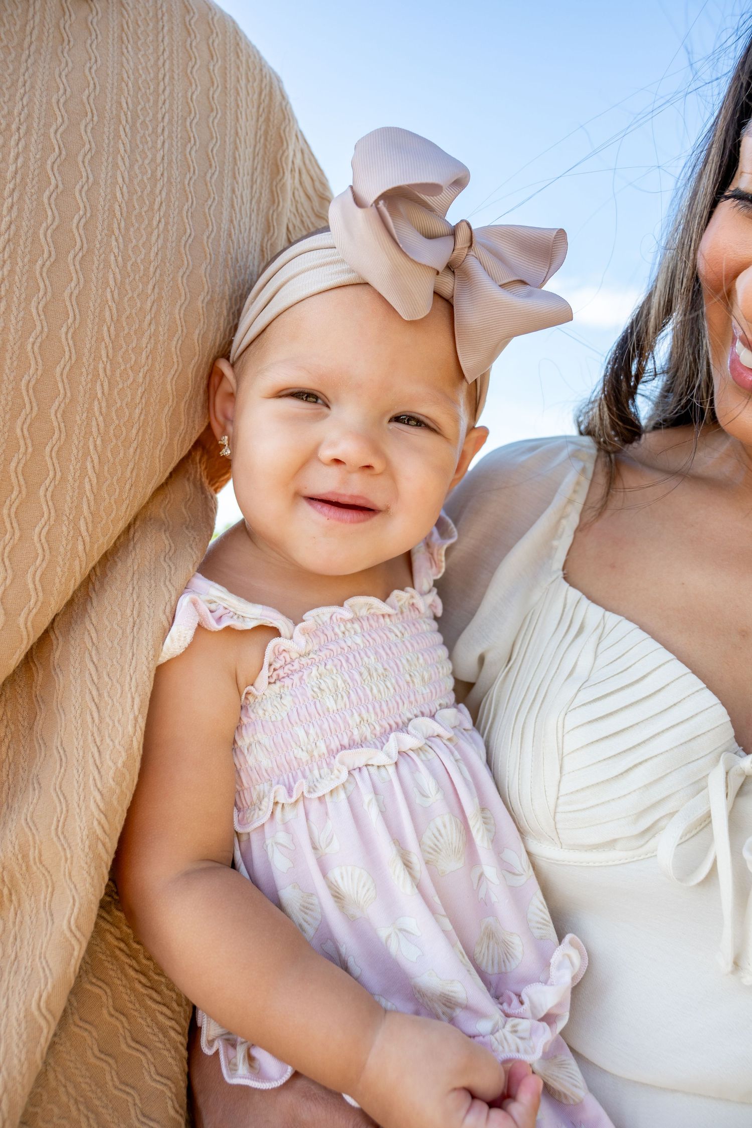 Baby wearing pink dress and white bow headband smiles at camera.