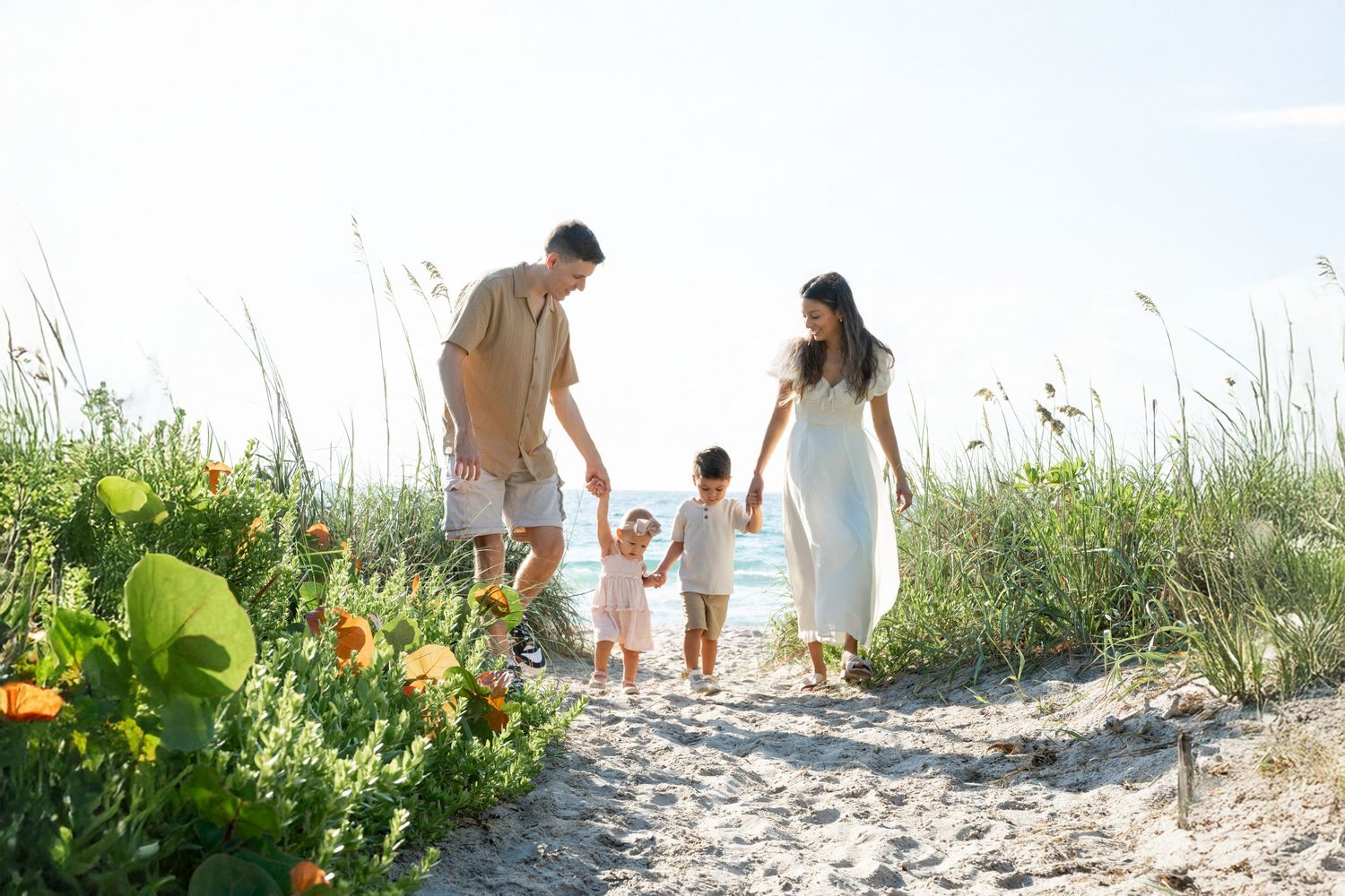 Family walking together on sandy beach path through coastal vegetation.