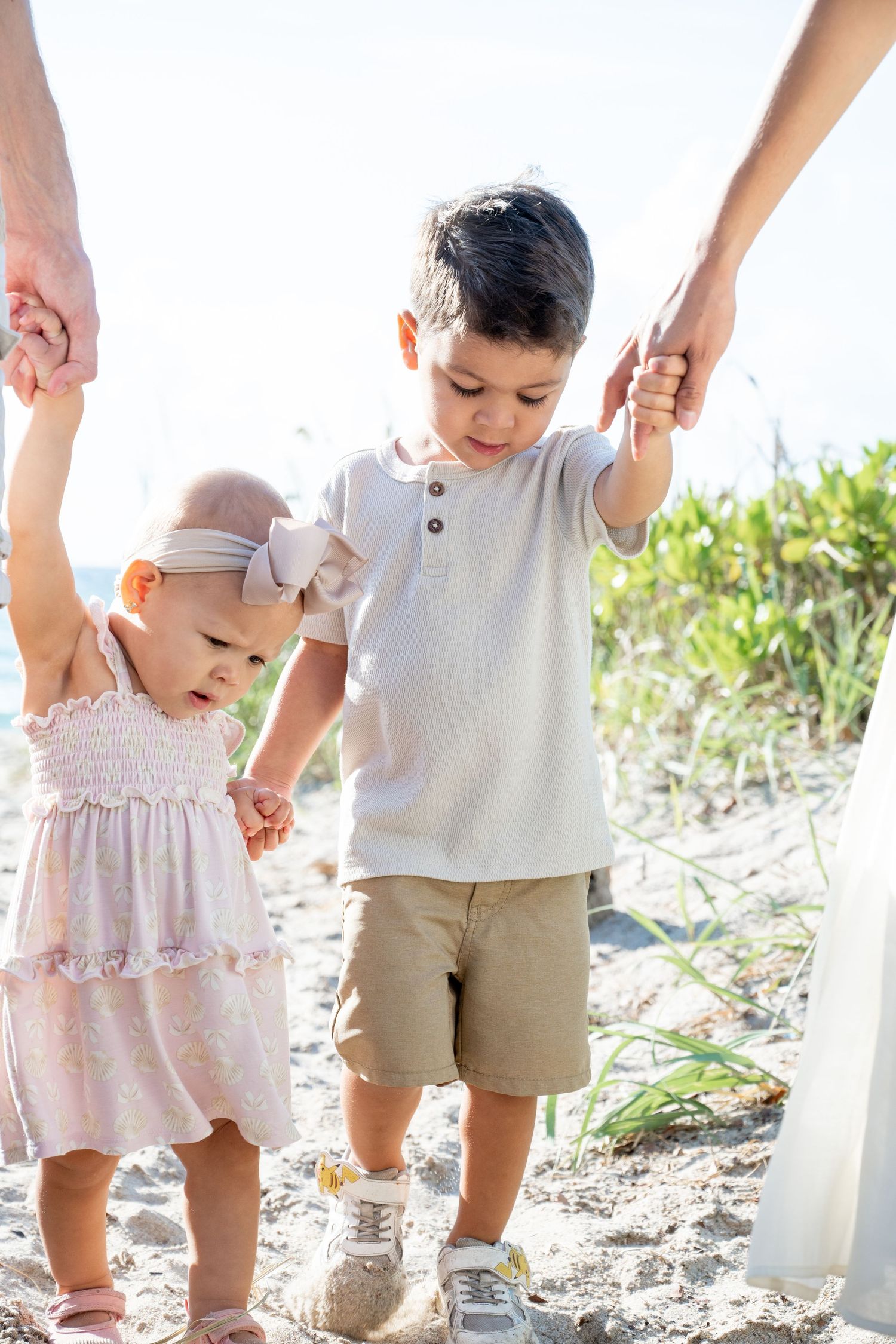 Two children holding hands while walking on sandy beach path.
