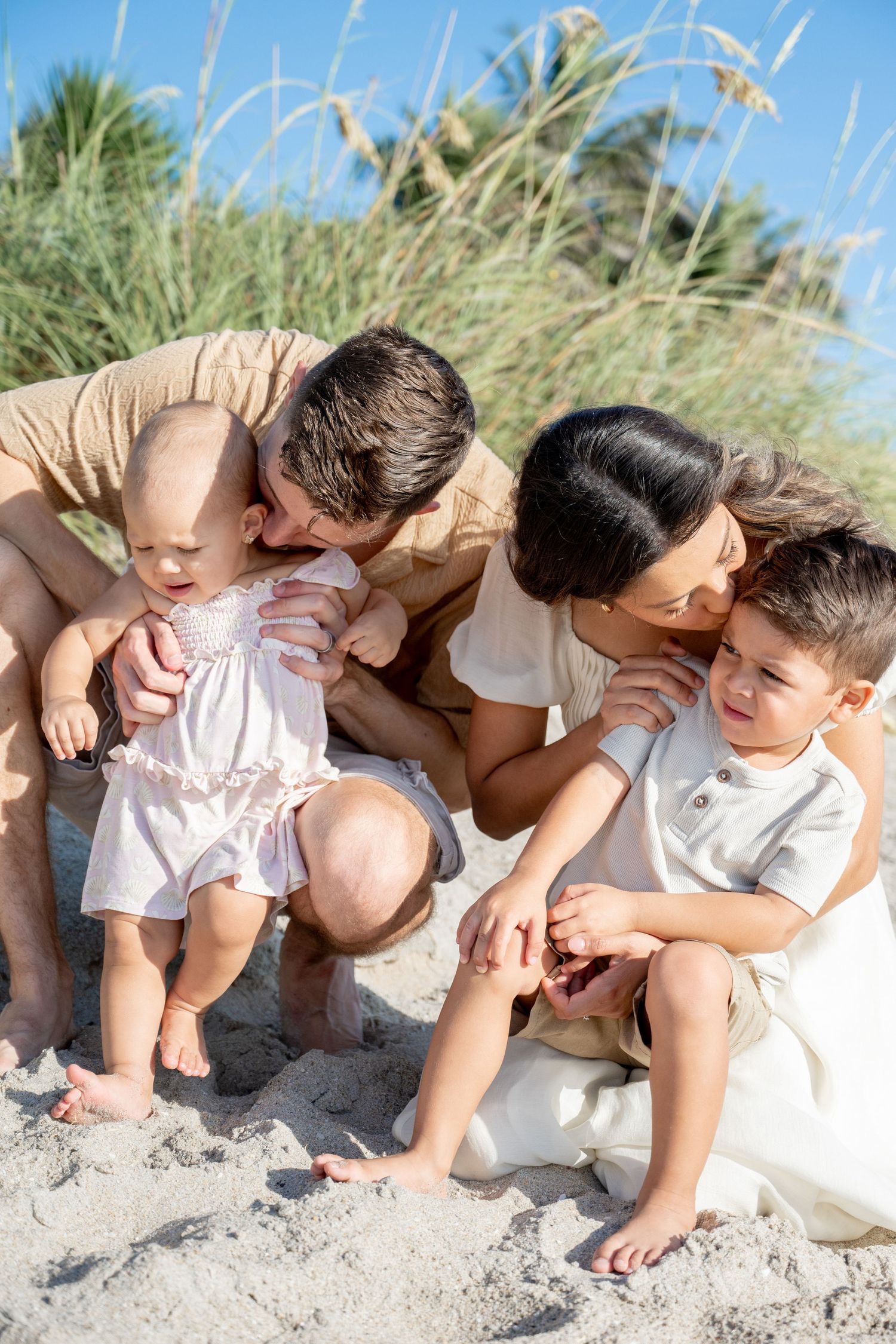 Family sharing intimate moment together on sandy beach with sea grass in background.