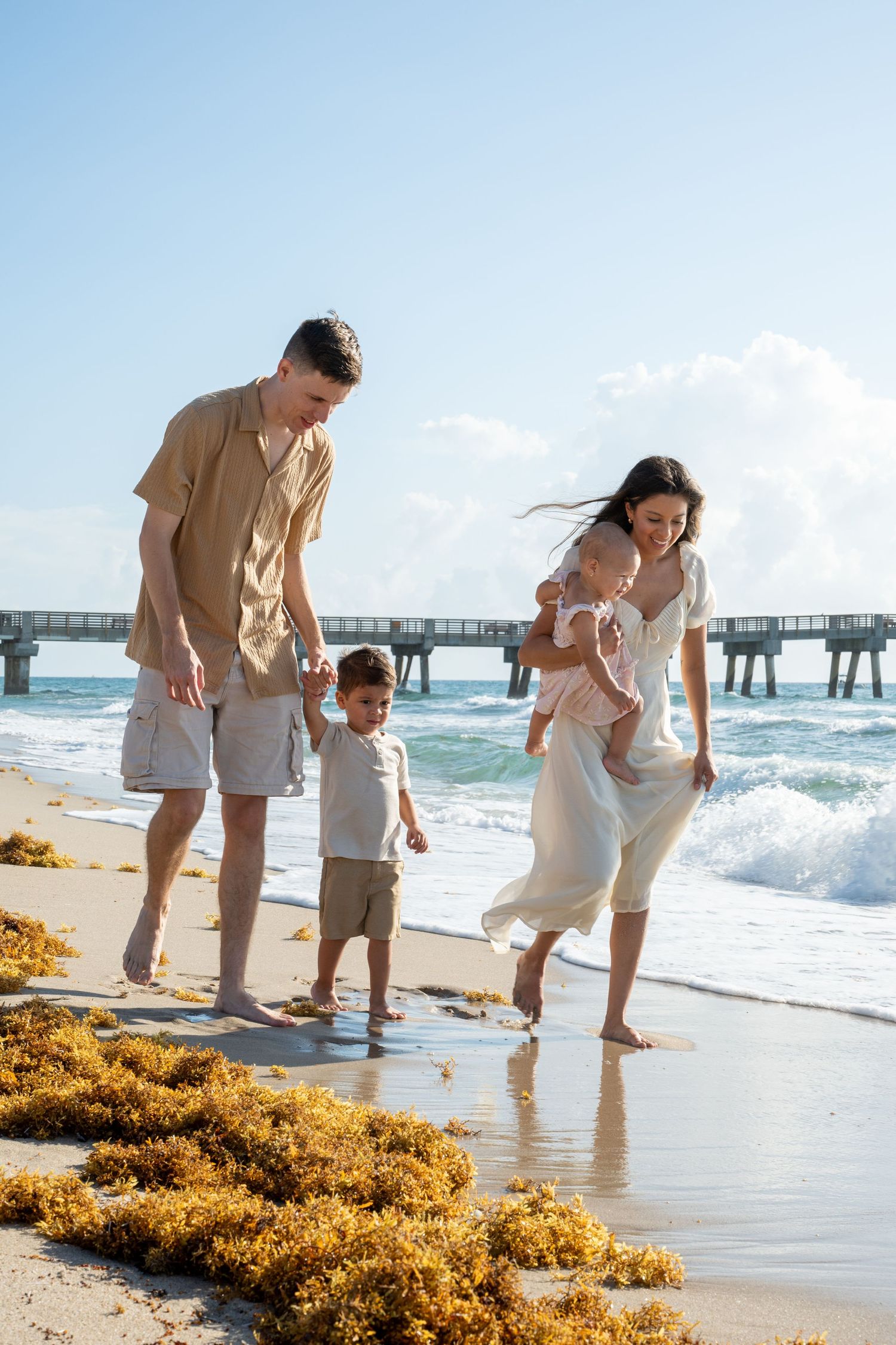 Family walking along beach shore near pier with waves rolling in.