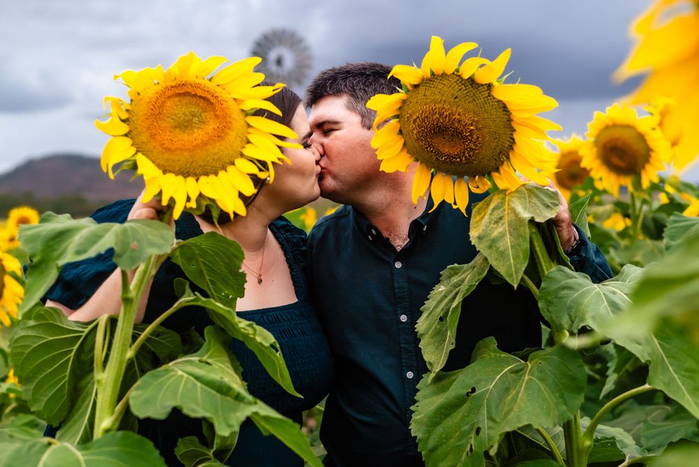 Couple sharing a romantic moment among blooming sunflowers against a cloudy sky.