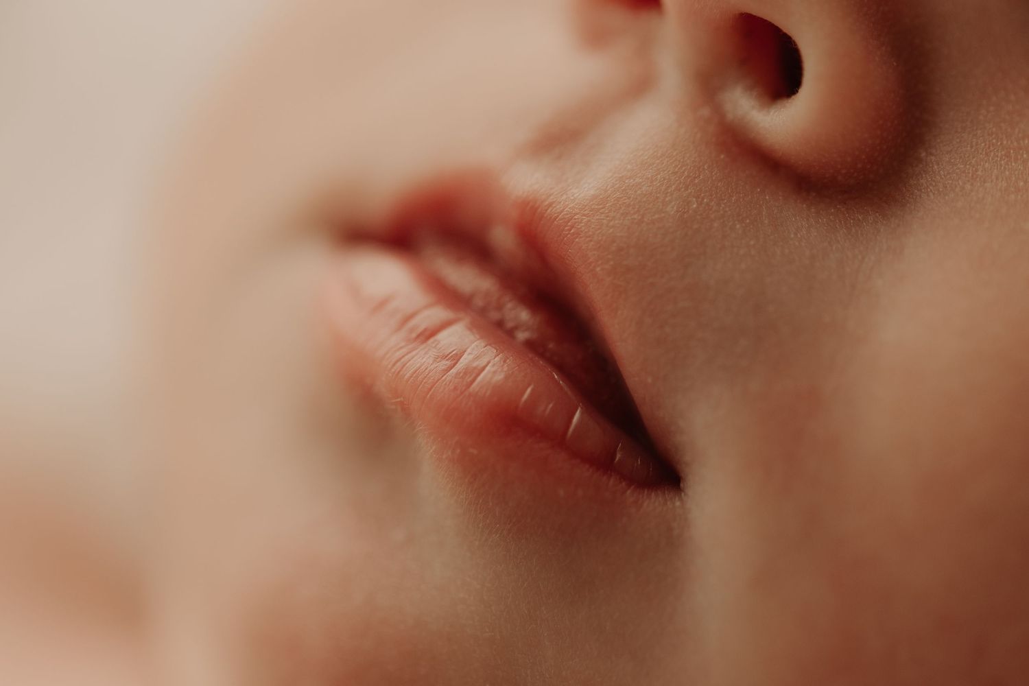 Macro photograph of newborn with pink lips against soft focus skin.