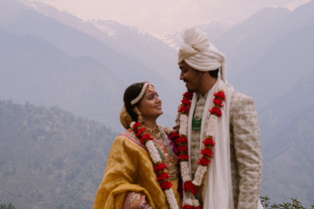 Couple in traditional Indian wedding attire sharing intimate moment against mountain landscape.