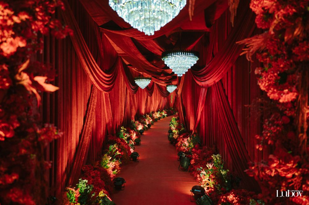 Luxurious red wedding decor with crystal chandeliers and floral arch.
