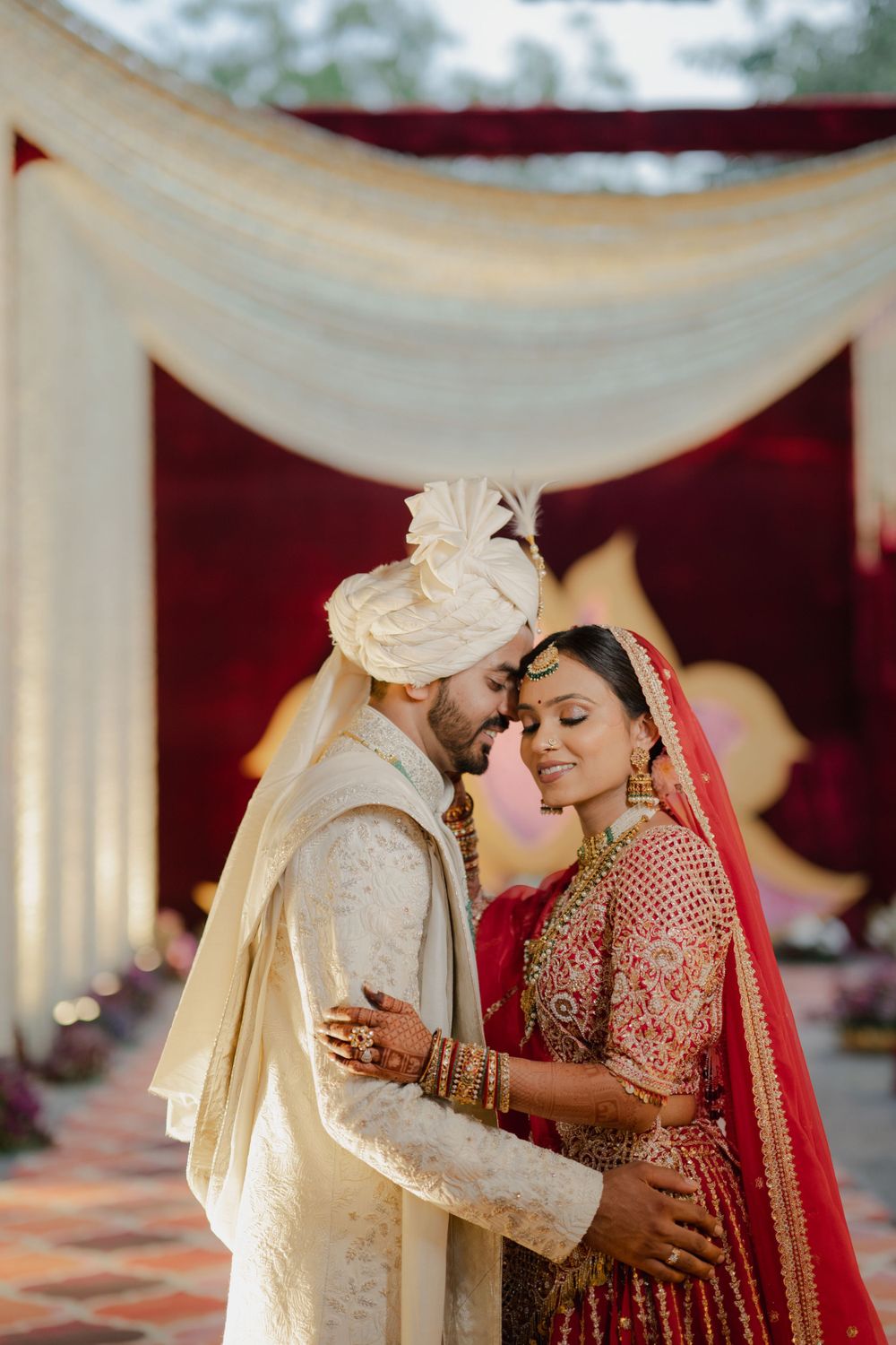 Intimate moment between newlyweds under white and red wedding mandap during Indian ceremony.