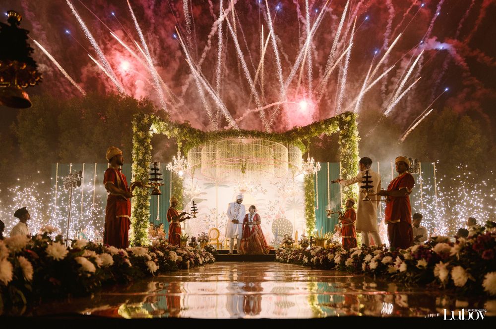 Stunning fireworks illuminate an outdoor wedding ceremony with a floral-adorned stage and crowd silhouettes.