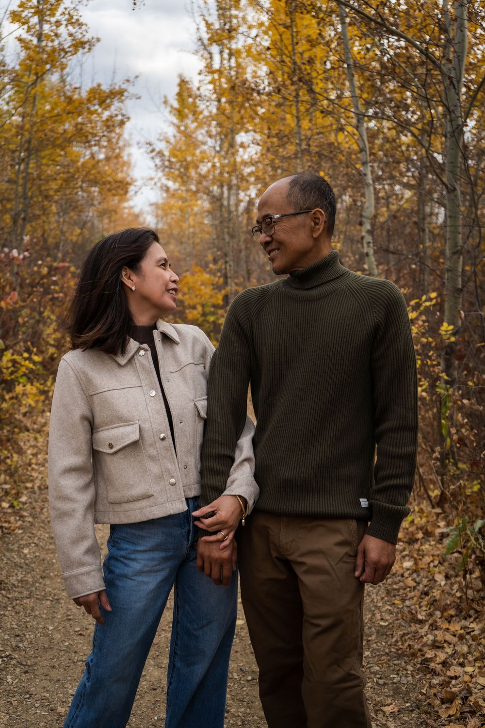 Couple sharing intimate moment on autumn path with yellow foliage in background.