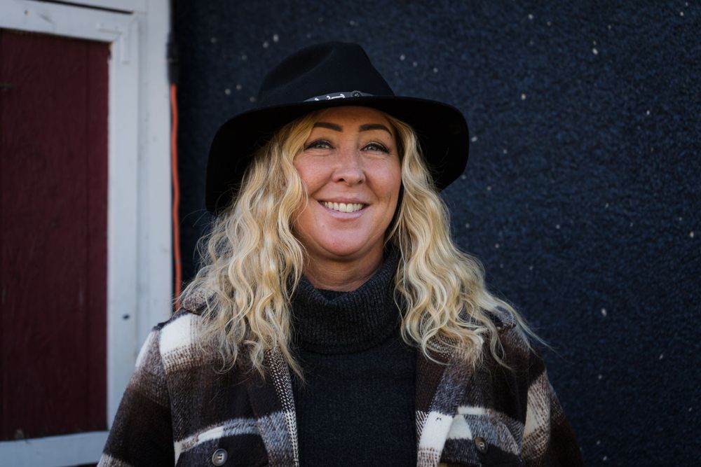 Woman in black hat and plaid coat smiling outdoors on a snowy day.