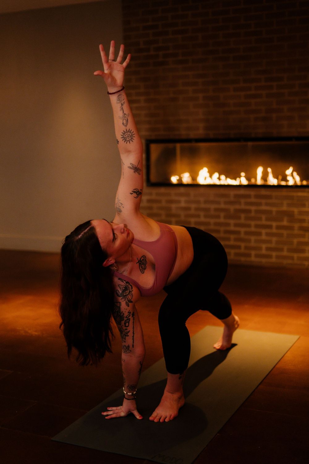 Yoga practitioner performing a twisting pose in front of a brick fireplace with ambient lighting.