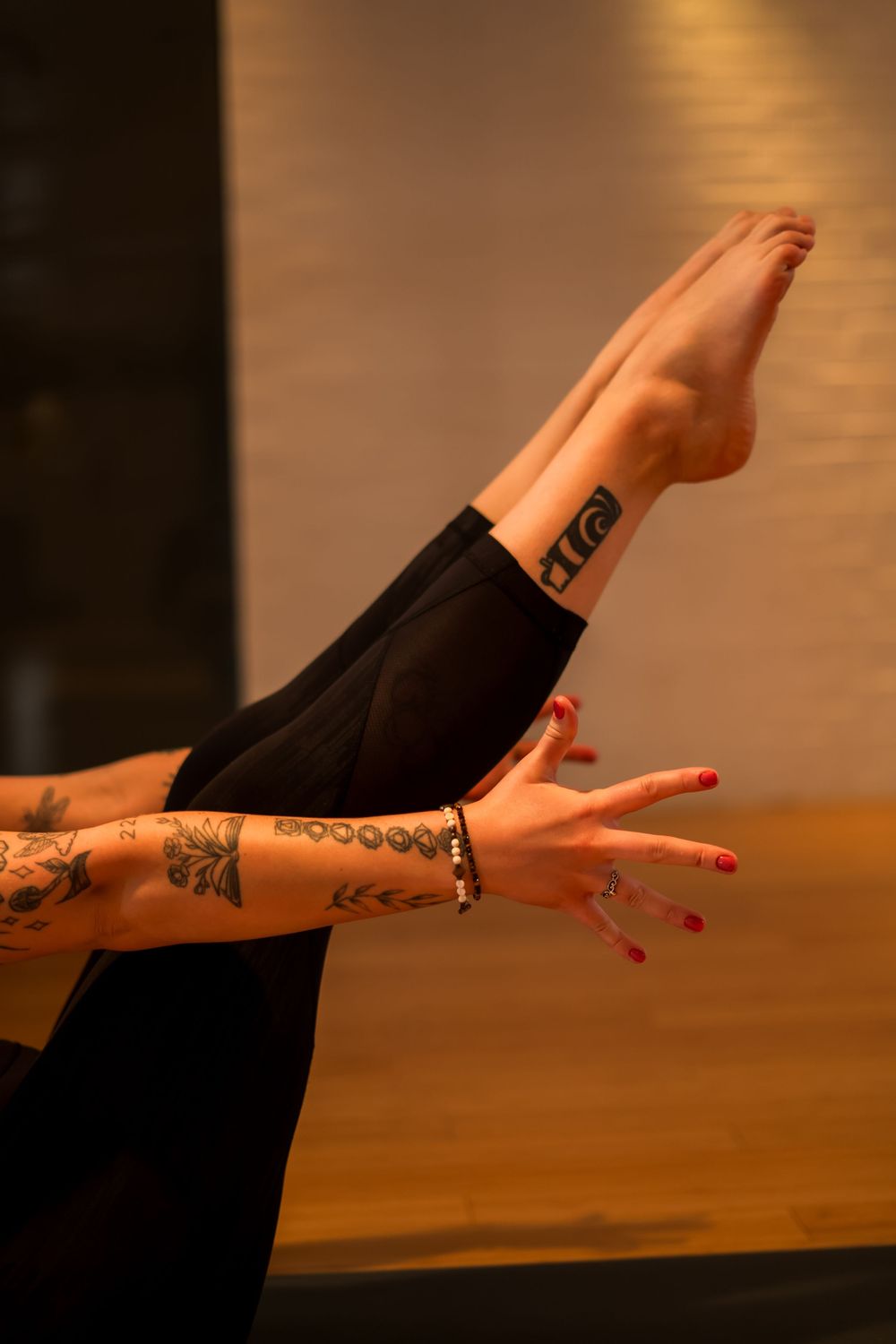 Tattooed arm and leg stretching during yoga pose against wooden floor background.