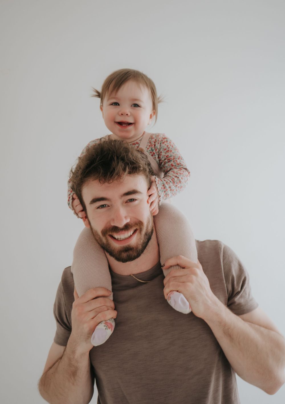 Joyful moment between parent and baby on shoulders against white background.