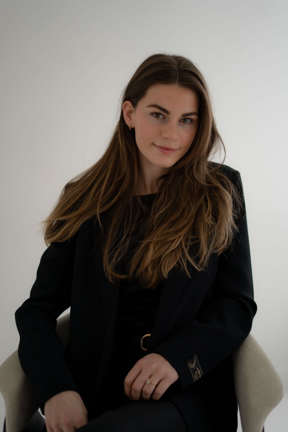 Professional studio portrait of someone with long brown hair wearing a black sweater seated against a white background.