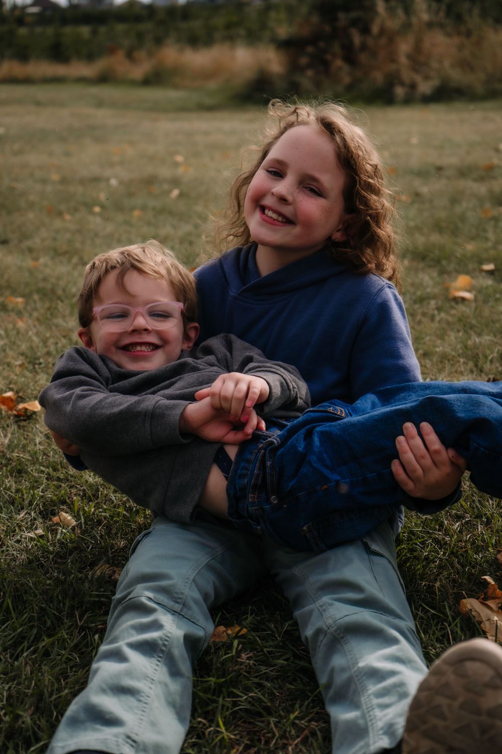 Two young children laughing and playing together on grass during fall.