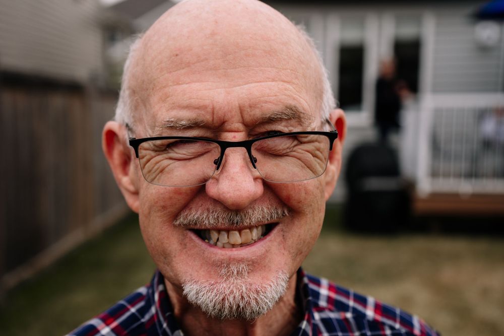 Portrait of a joyful senior man with glasses and a plaid shirt smiling at the camera.