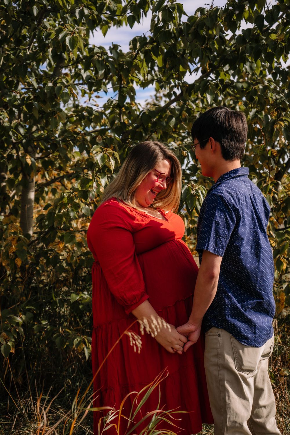 Family photo session against autumn trees with red and blue coordinated outfits.