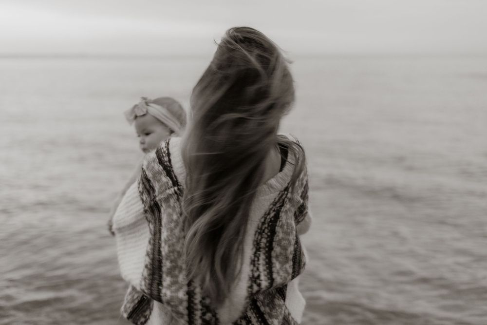 Long hair blowing in the wind against an overcast ocean backdrop creates a dreamy silhouette.