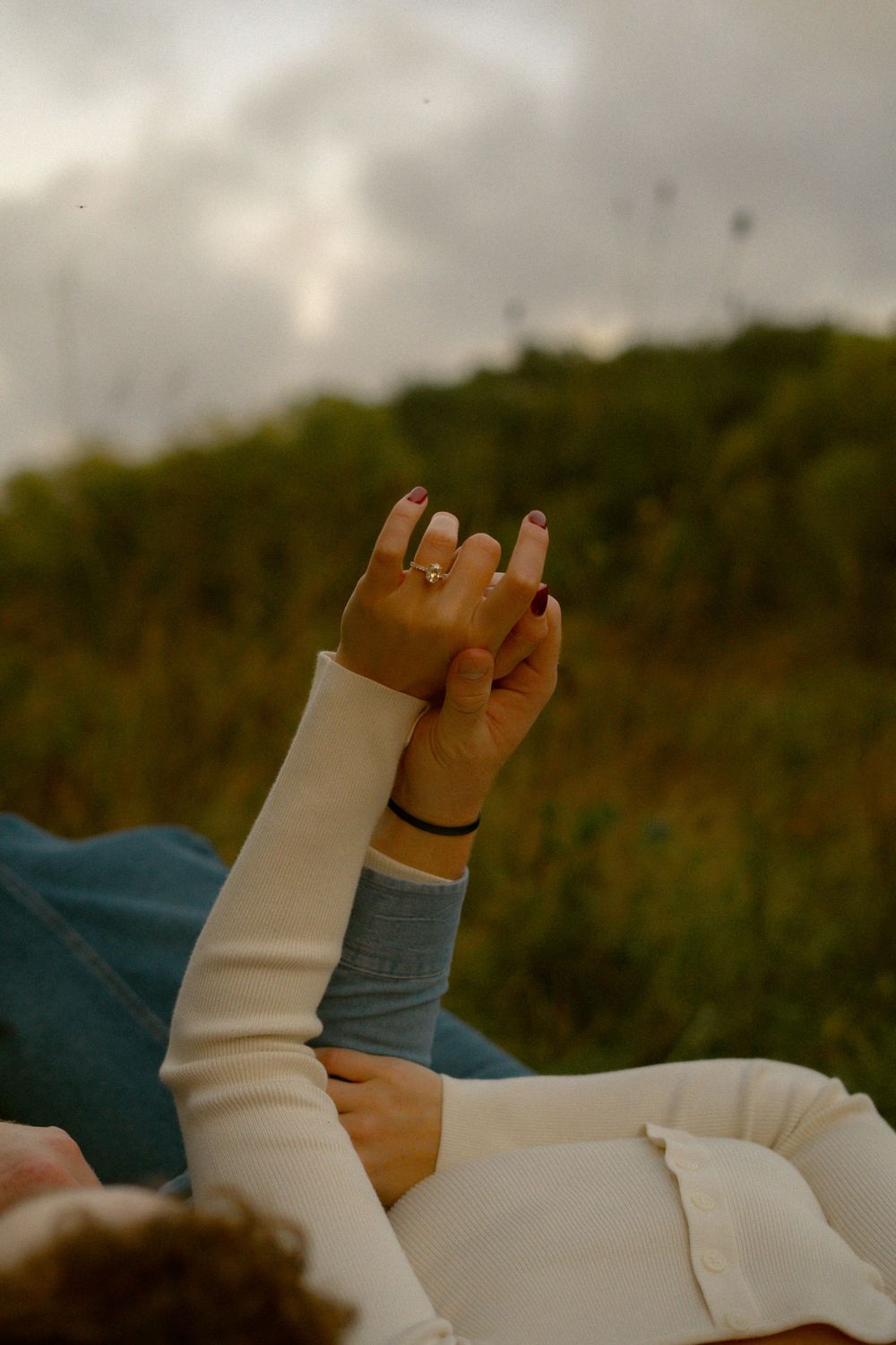 Hand displaying engagement ring against blurred natural background during golden hour.