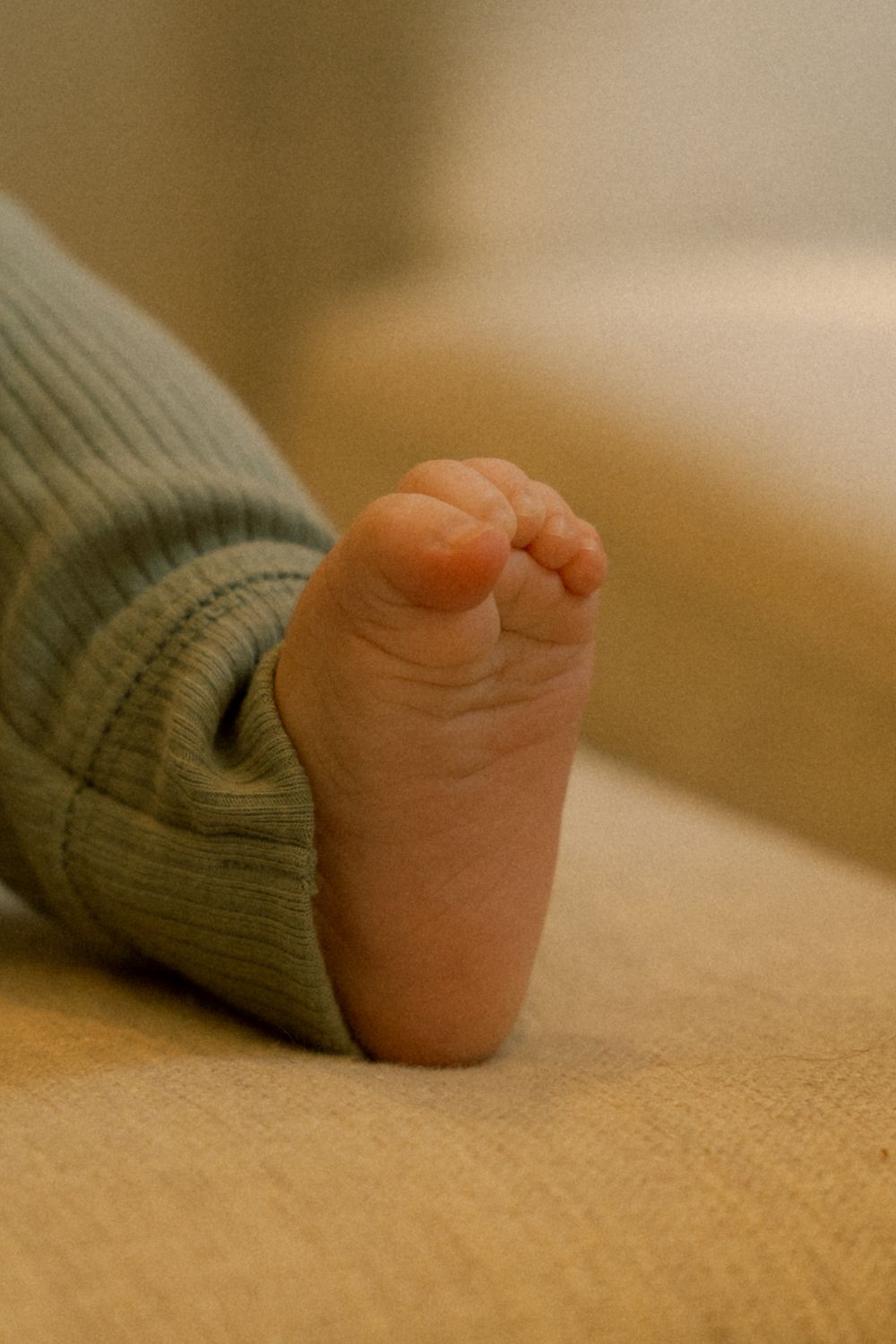 Close-up of a tiny baby foot in a green sweater resting on a beige surface.