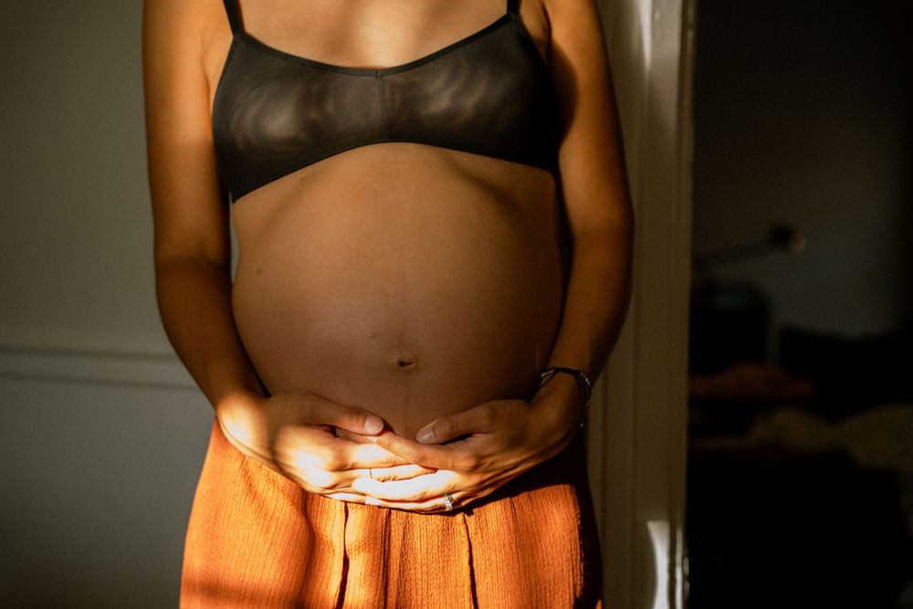 Close up of a pregnant belly in orange lighting with hands cradling the bump.