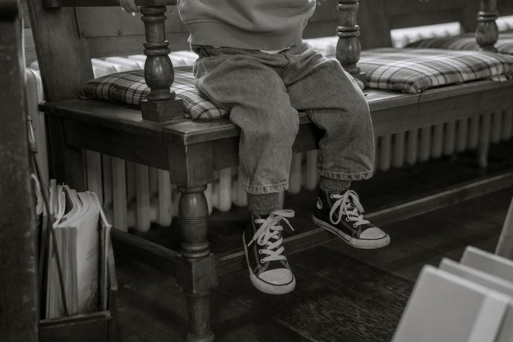 A black and white close-up of small feet in sneakers sitting on a wooden bench.
