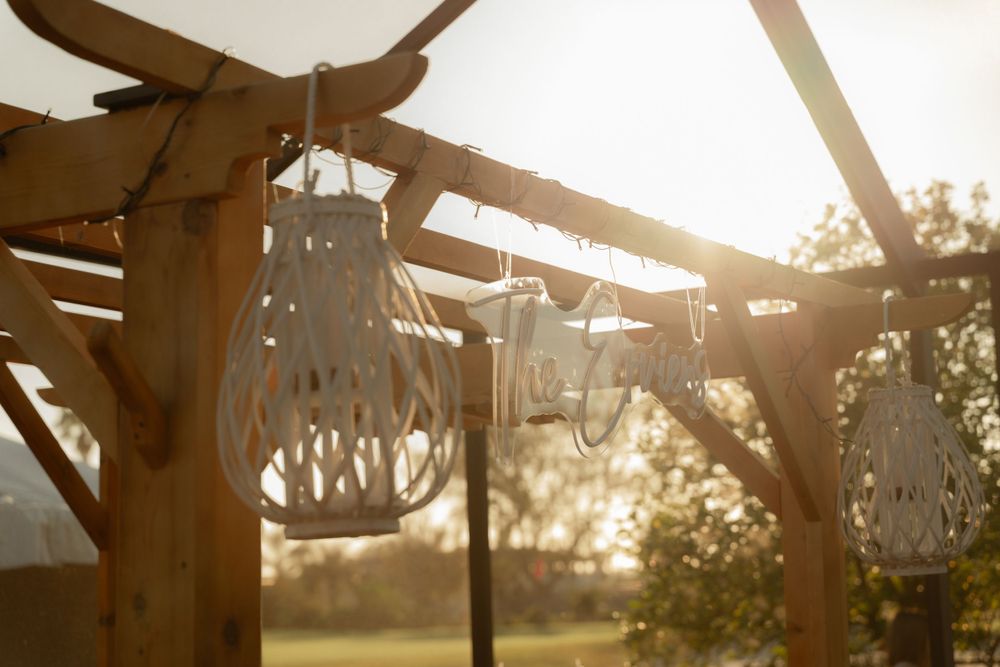 Sunlight streaming through wooden beams and woven lanterns at an outdoor wedding ceremony setup — warm, golden, and romantic.