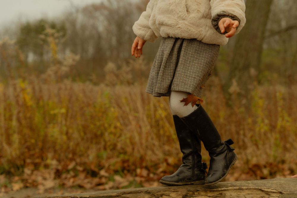 Cropped view of legs wearing black boots and a knit skirt against an autumn landscape.