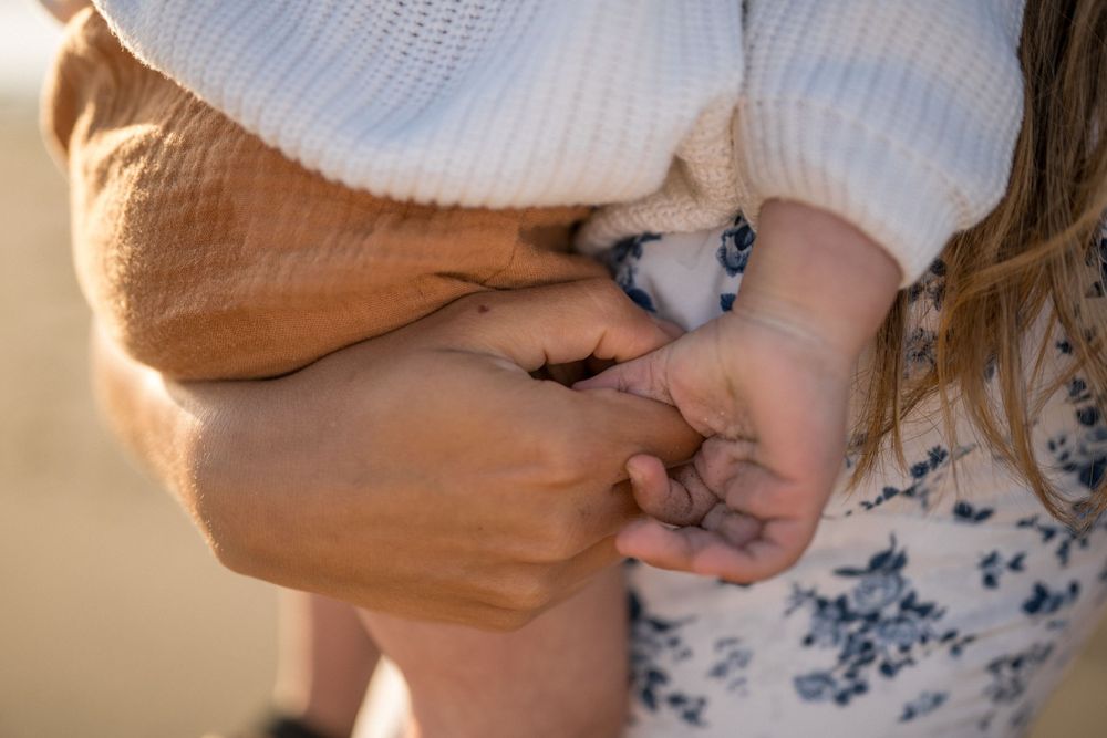 Close-up detail of hands touching against a blurred beach background at sunset.
