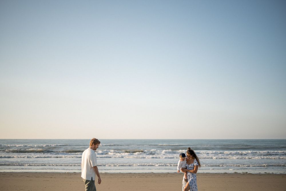 Two people walking on a sandy beach with ocean waves in the background.