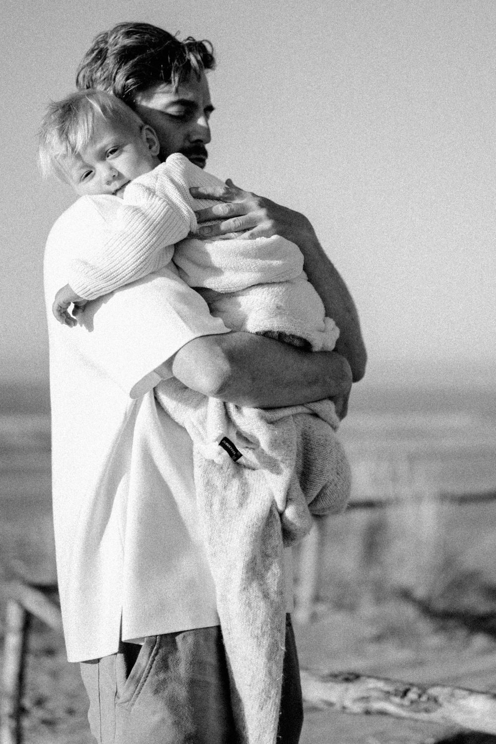A tender embrace captured in black and white against an ocean backdrop.