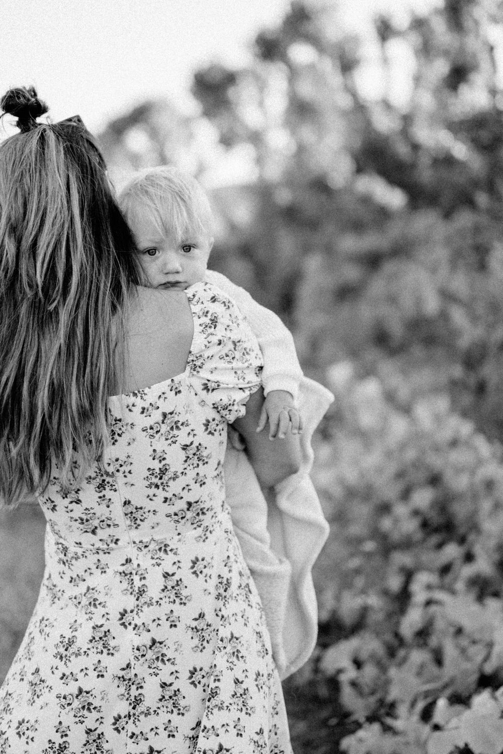 Black and white portrait of a small child being held in a floral dress outdoors.