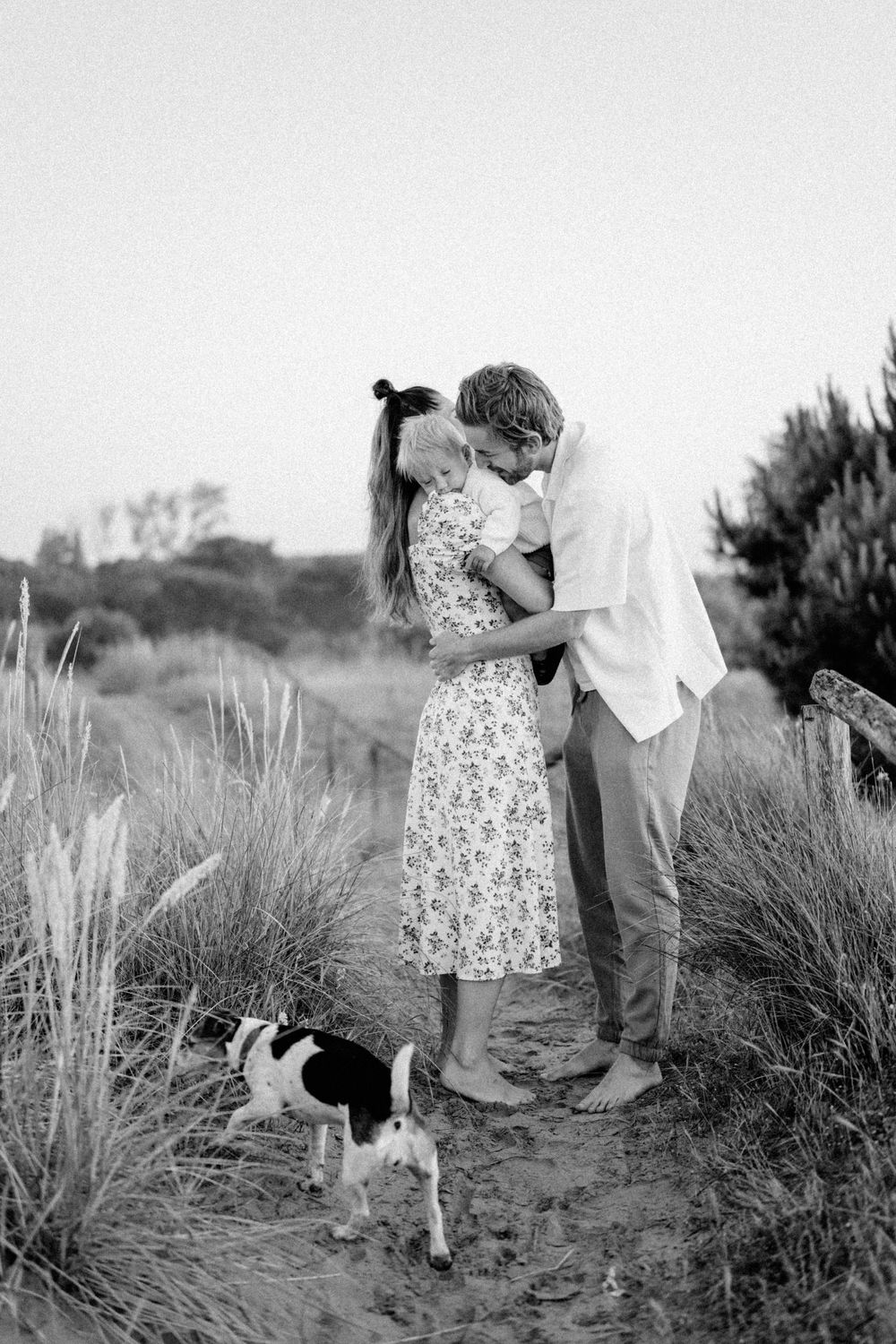 A romantic moment captured in black and white on a coastal path with a small dog nearby.
