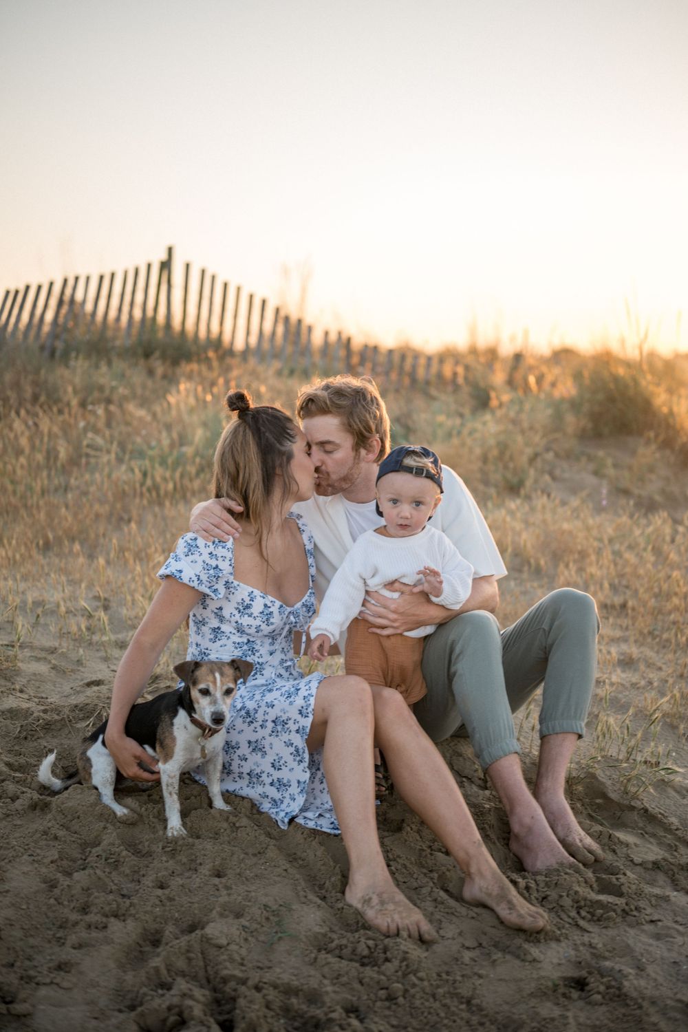 Family sitting together on sandy dunes with their pet dog at sunset.