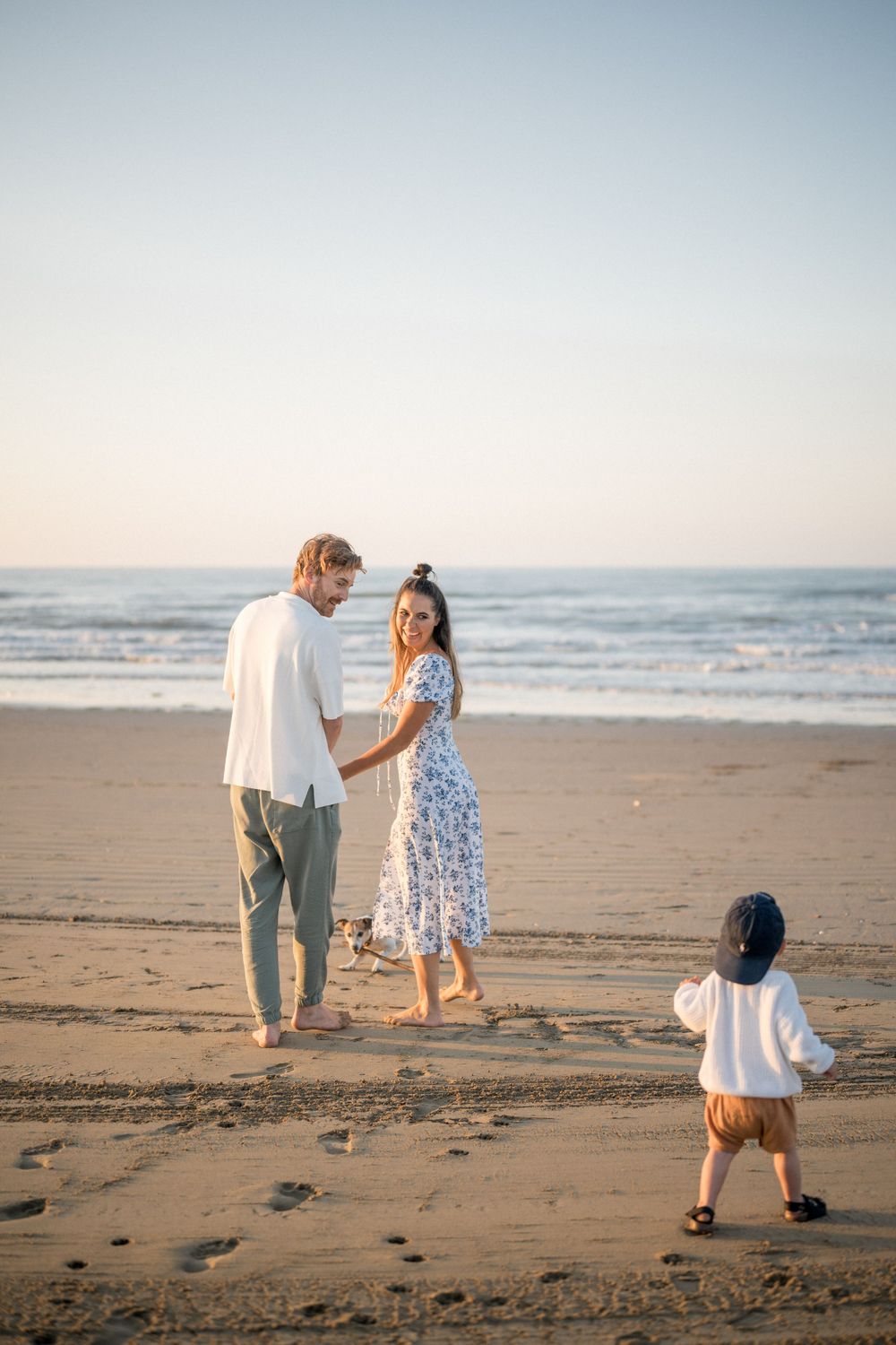 Family walking together on beach at sunset with toddler following behind.