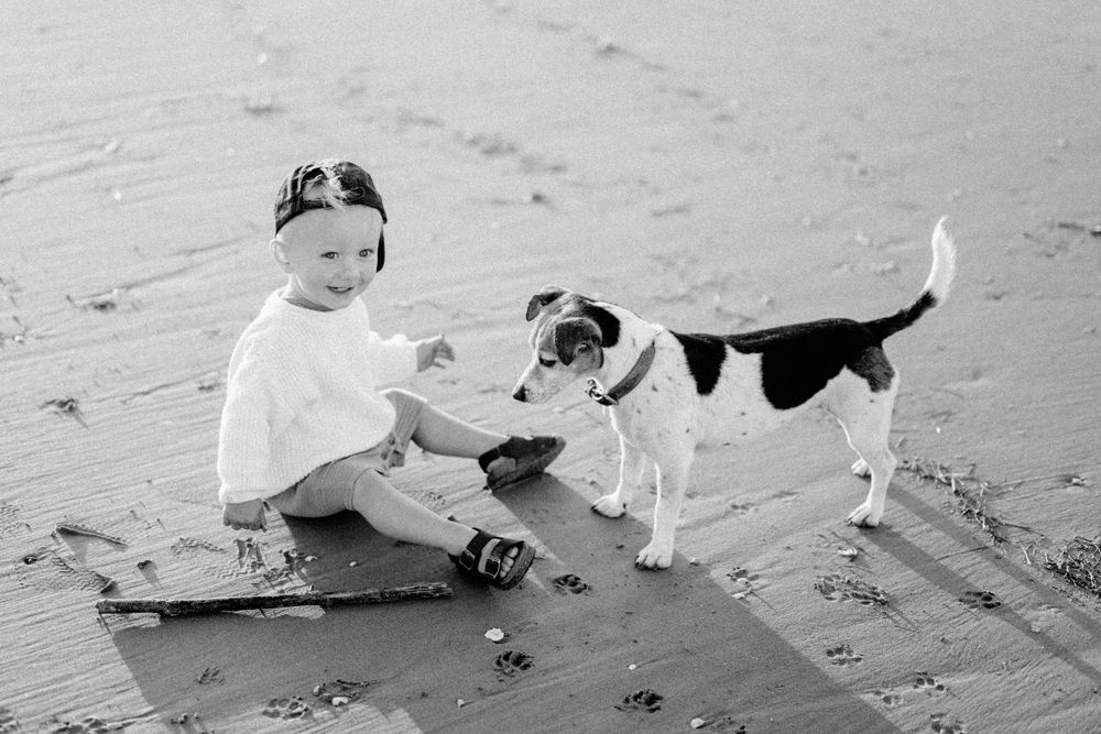 A child plays with their dog on the sandy beach in a joyful black and white moment.