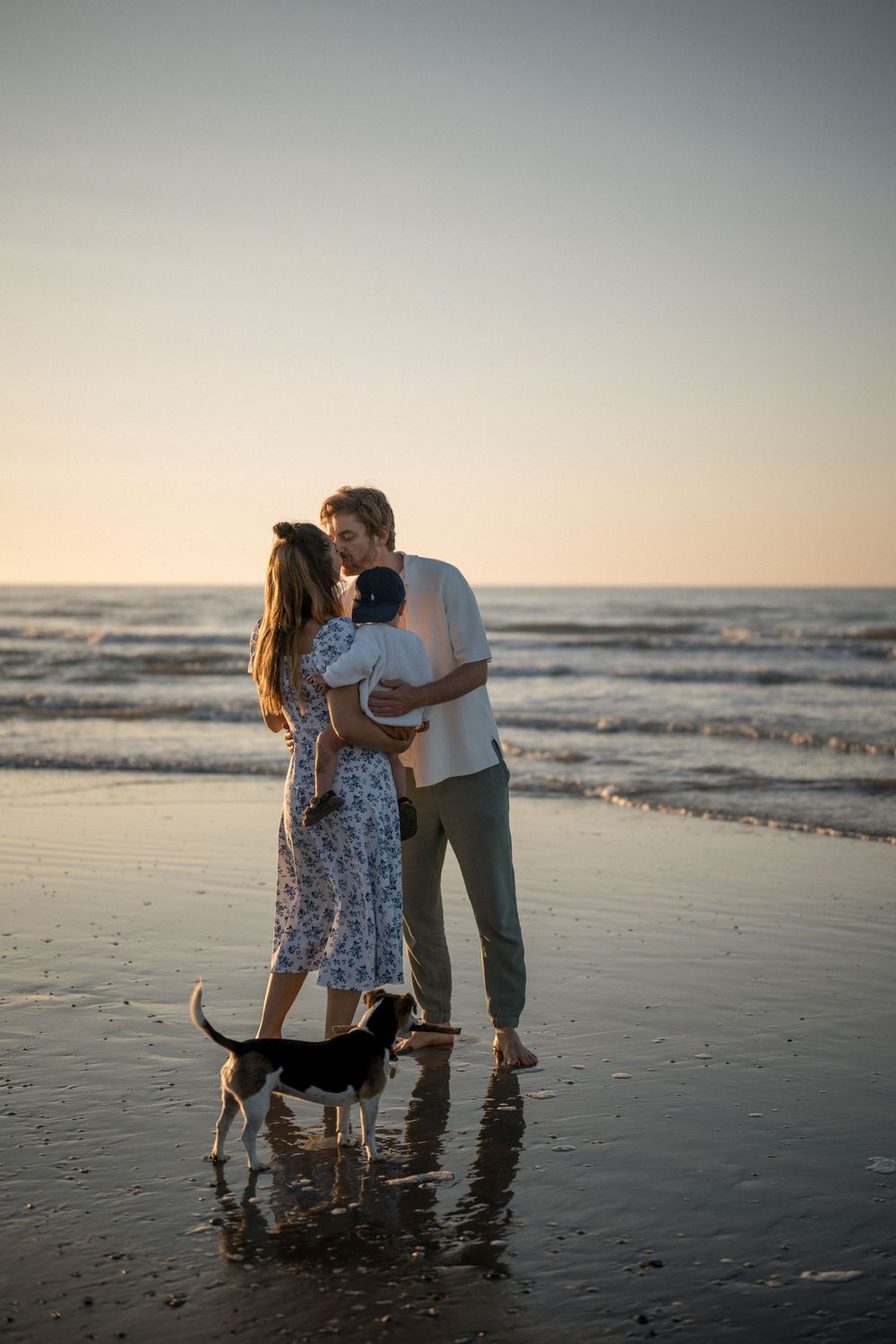 A romantic sunset beach moment with a small dog playing in the waves nearby.