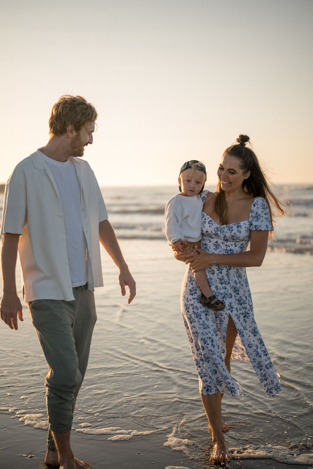 A family walks together along a peaceful beach at sunset with waves rolling in.