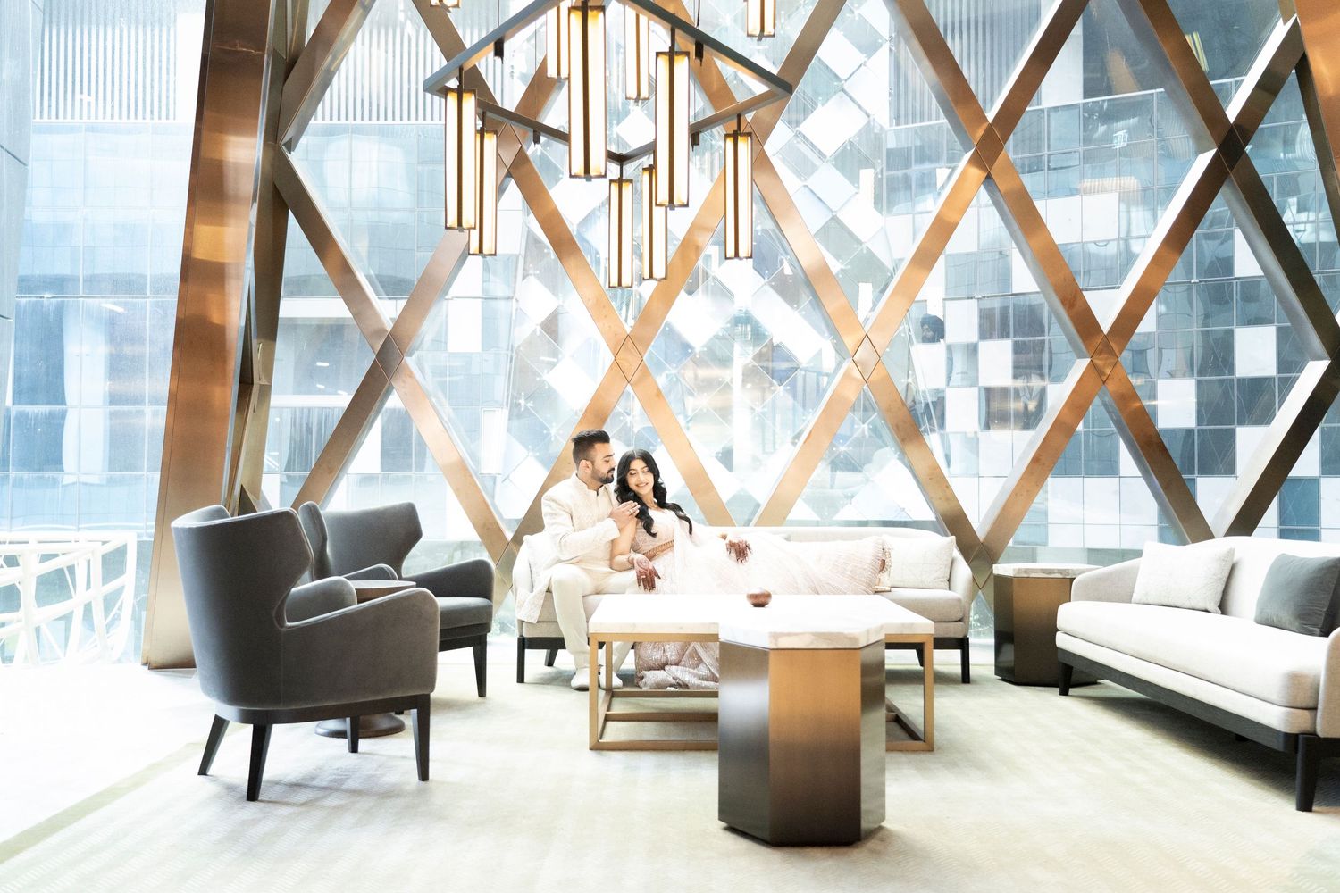 Modern lounge area with geometric window design, grey armchairs, and light streaming through latticed windows.