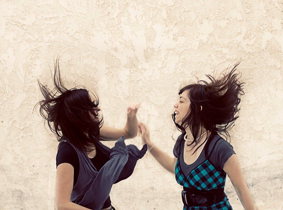 Artistic photo of two people with windswept hair high-fiving against a beige background.