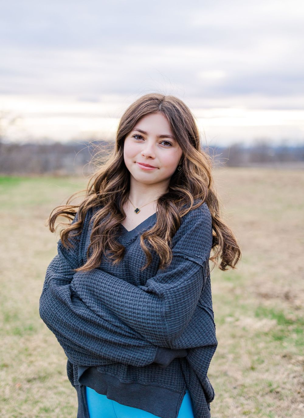 A person in a navy sweater and bright blue leggings stands in an open field at dusk.