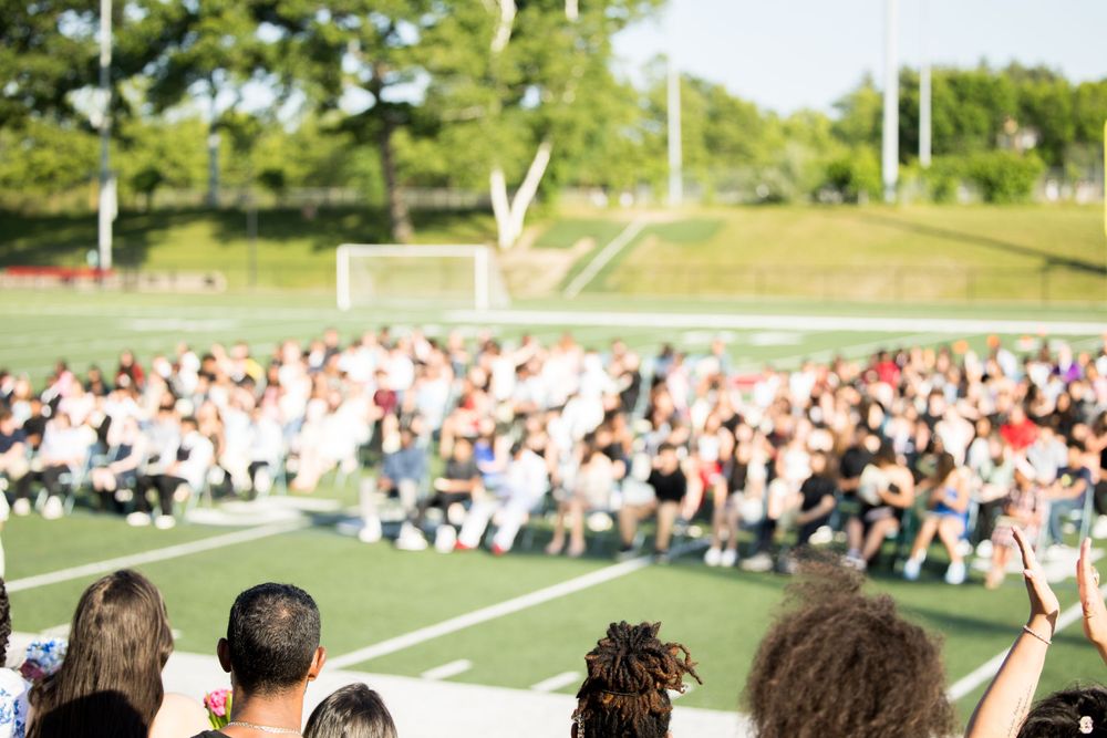 A crowd of spectators seated in bleachers watching an outdoor event on a sunny day.