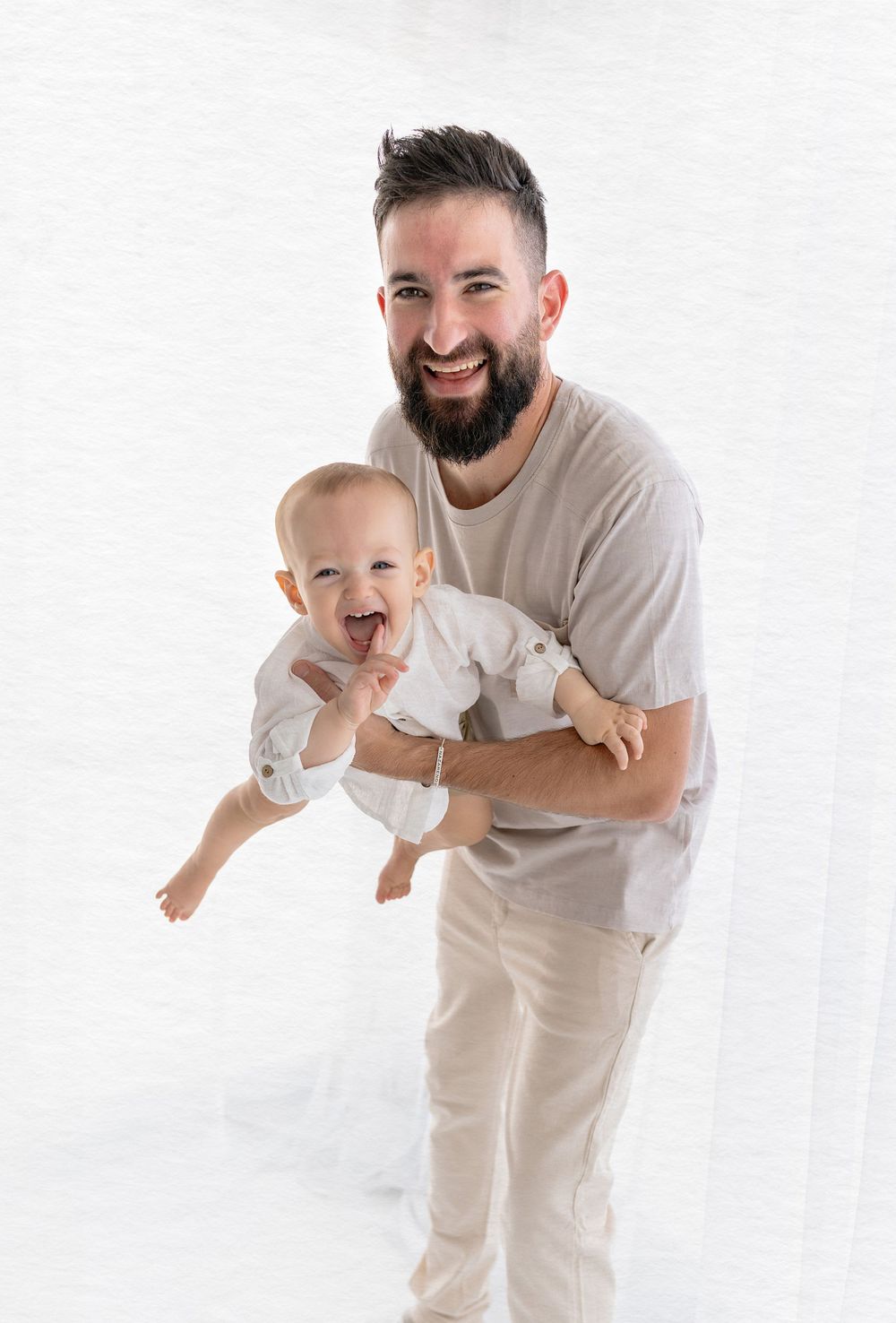Parent playfully holding a joyful baby in a bright studio setting with white background.