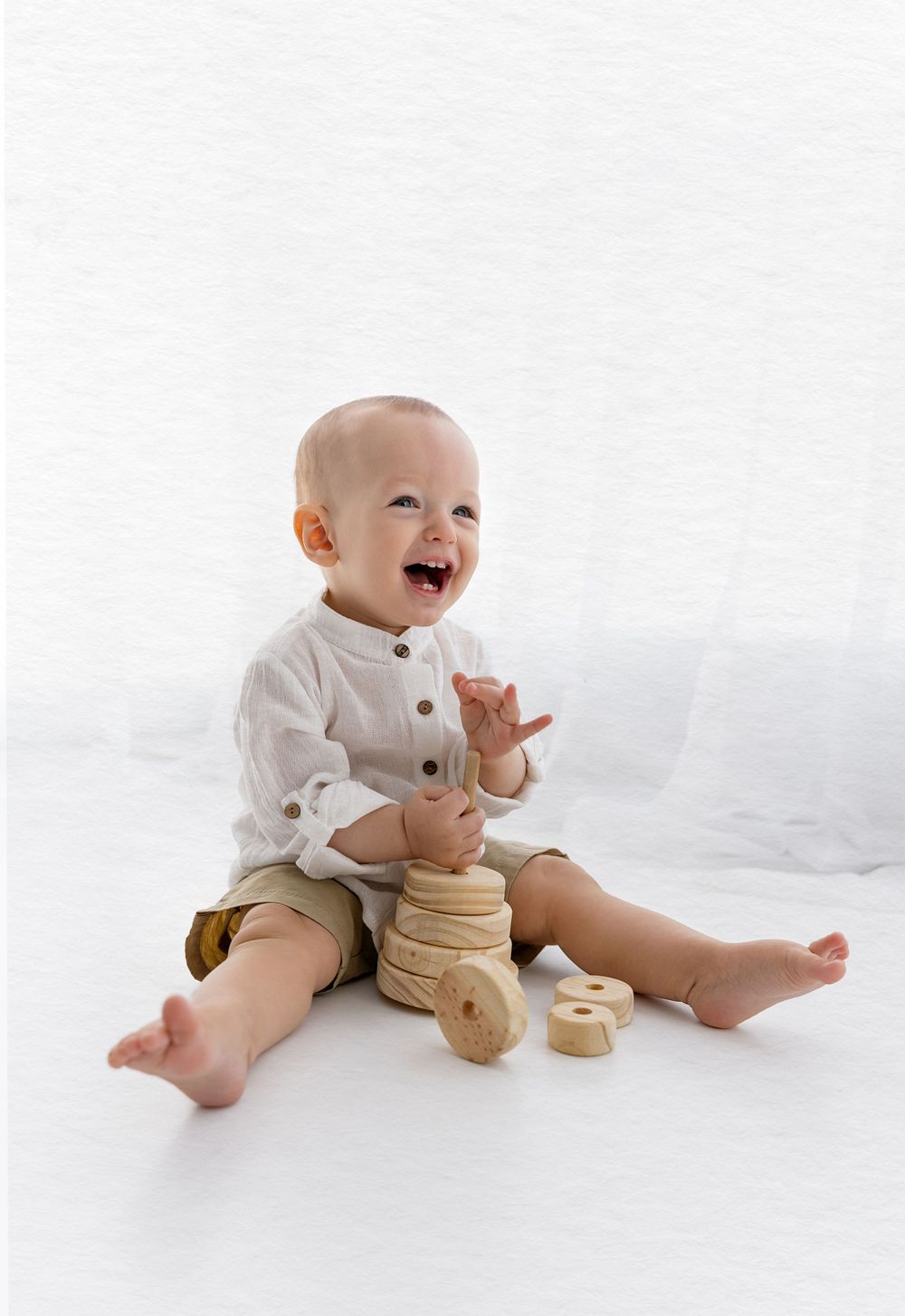 Joyful baby in white shirt plays with wooden stacking toys.