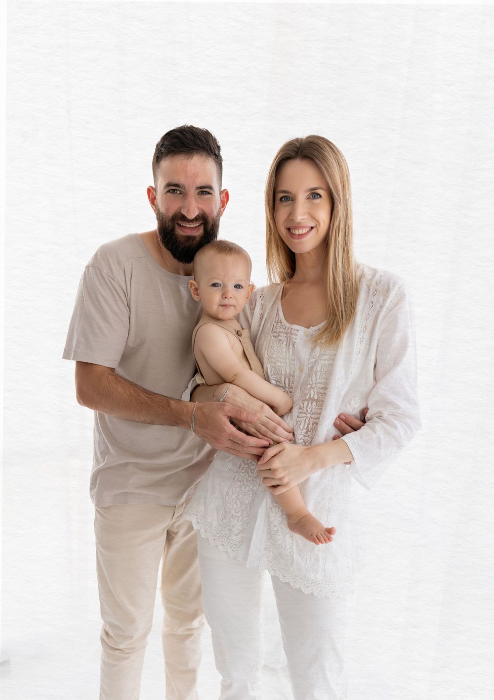 Family in neutral colors poses together against white background.