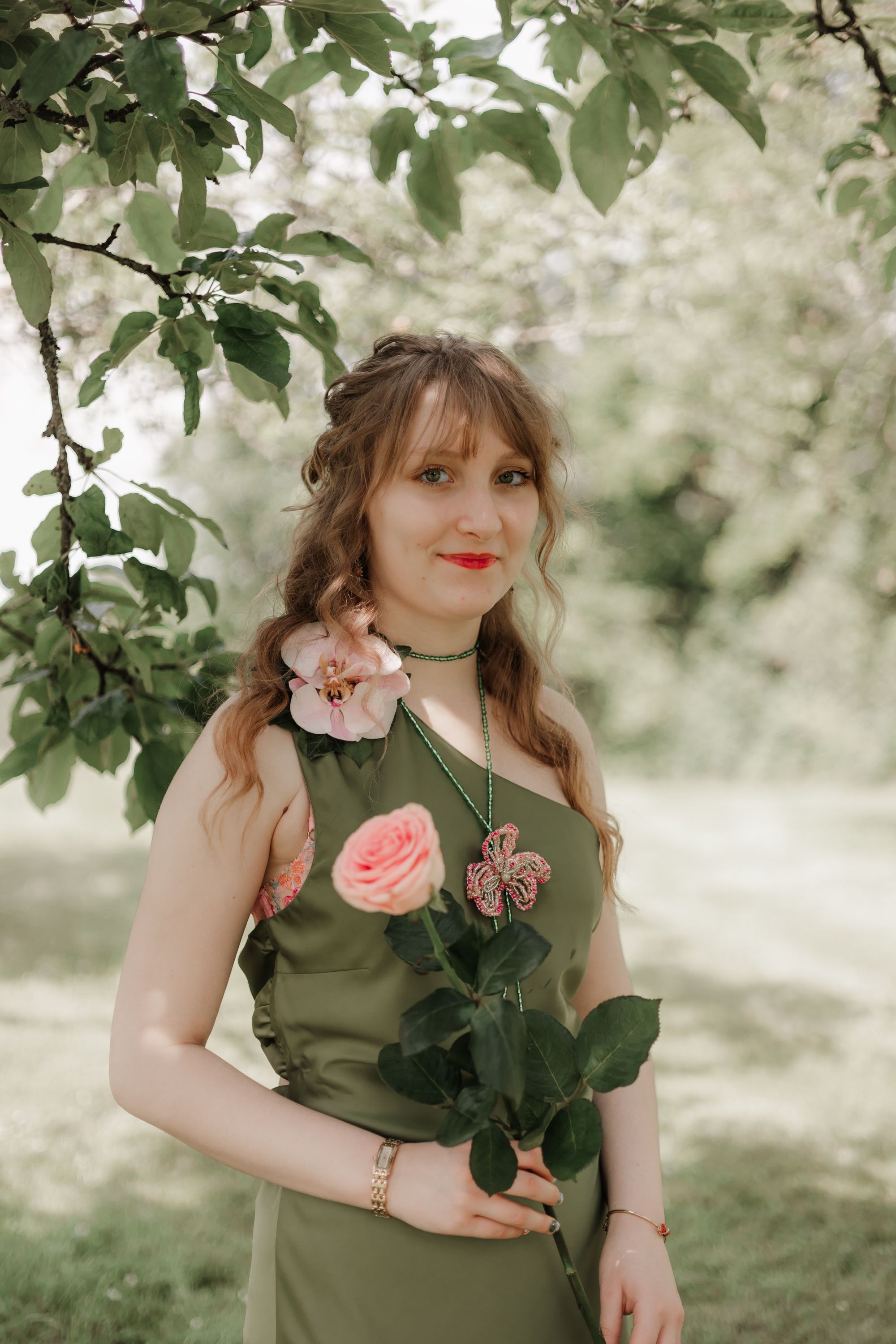 Person in olive green dress posing with roses in garden setting.