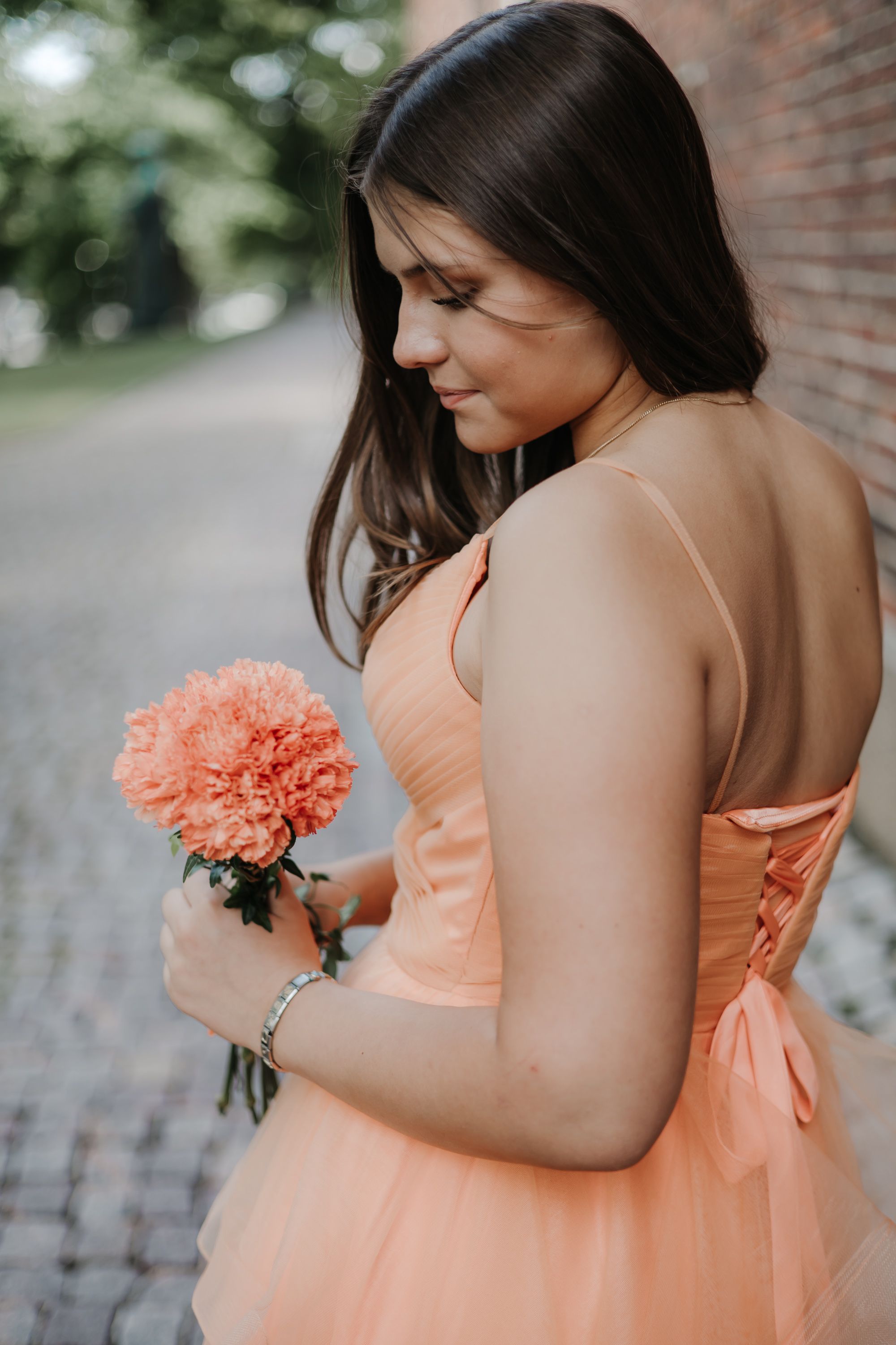 Bridesmaid in peach dress poses with coral flowers against brick wall.