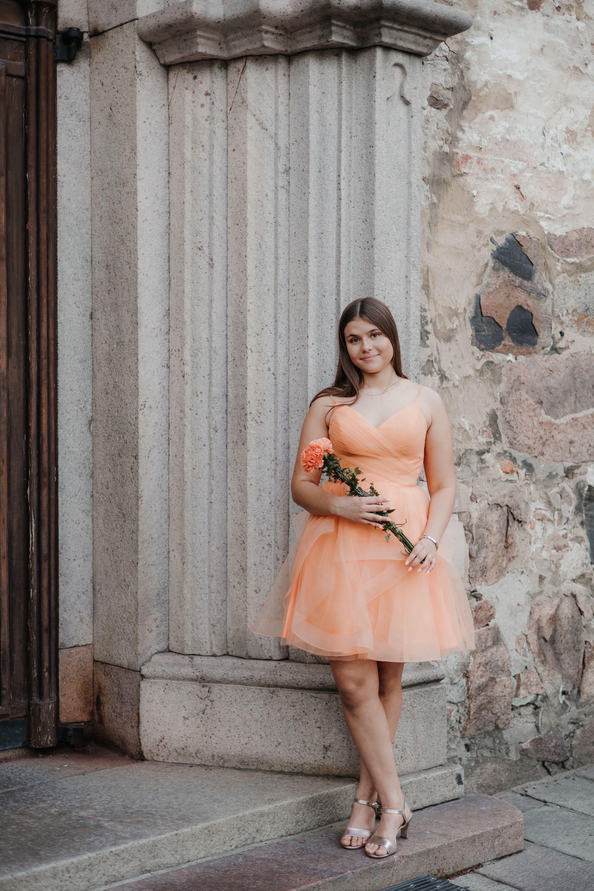 Person in peach dress posing against weathered stone wall architecture.
