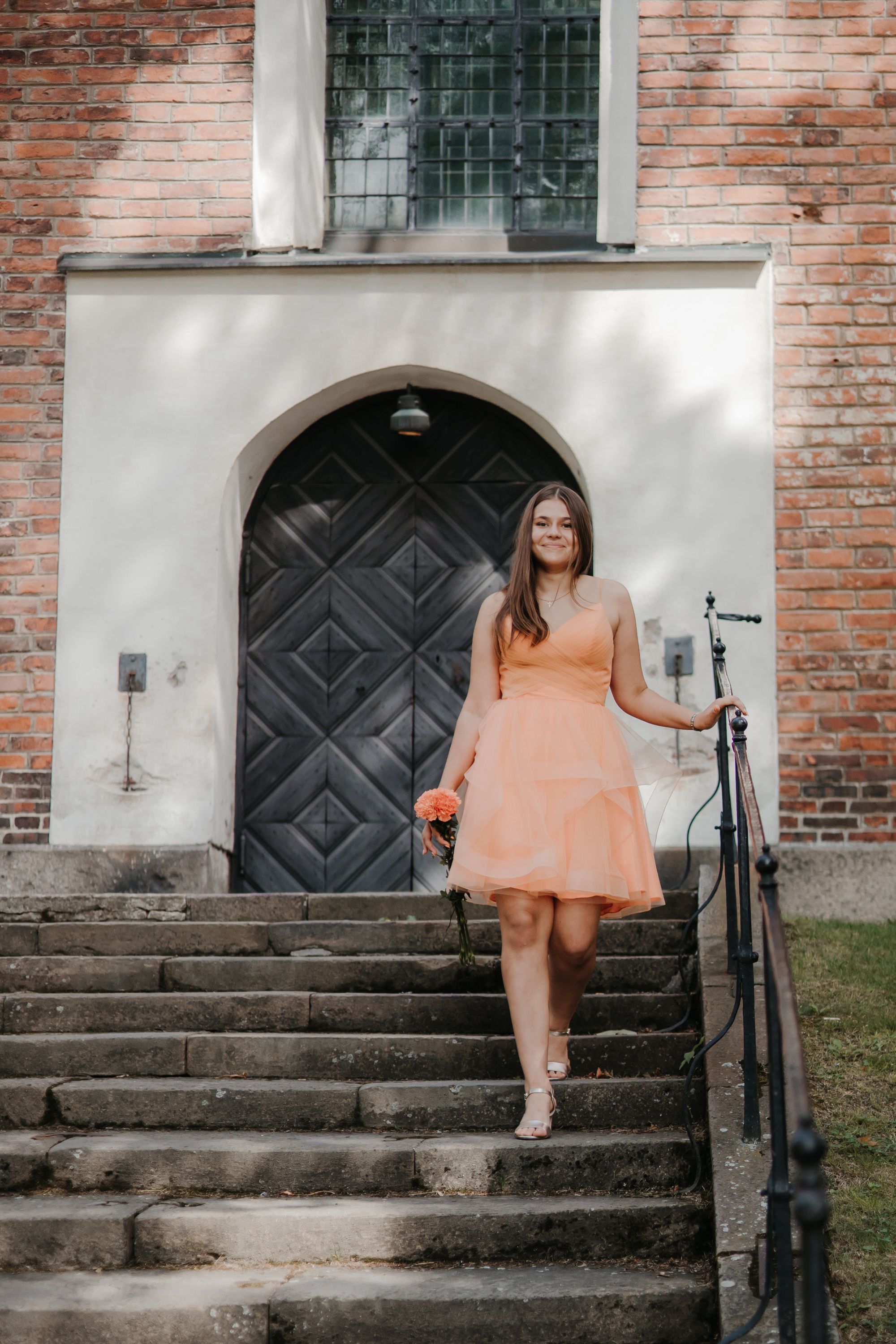 Person in peach dress sitting on historic brick building steps.