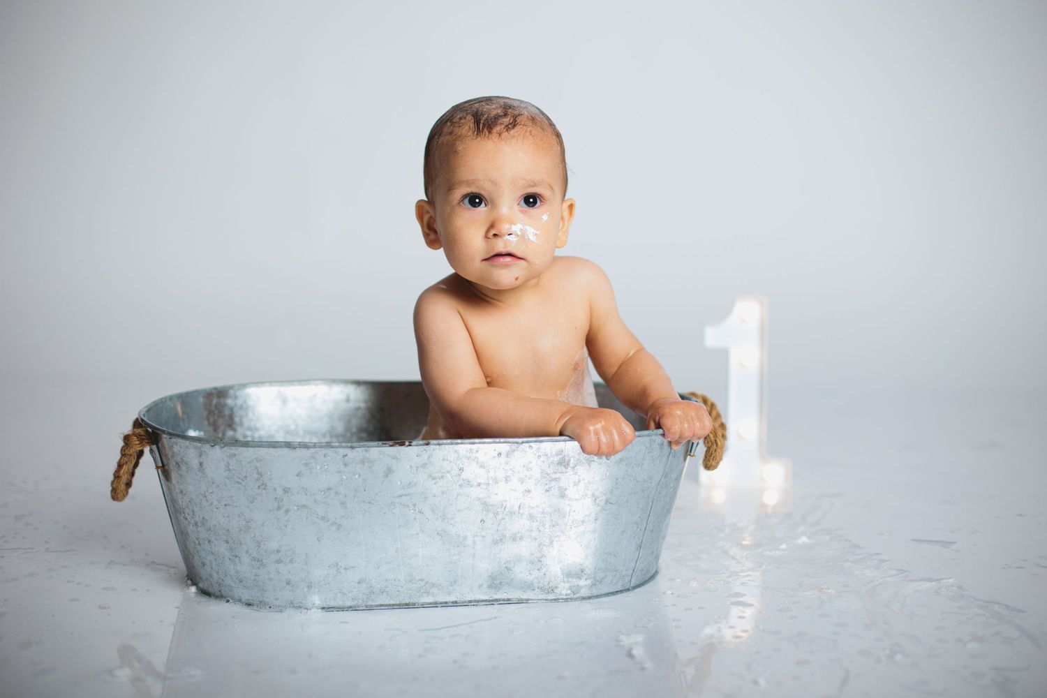 Baby sits in vintage metal tub with number one candle for first birthday portrait session.