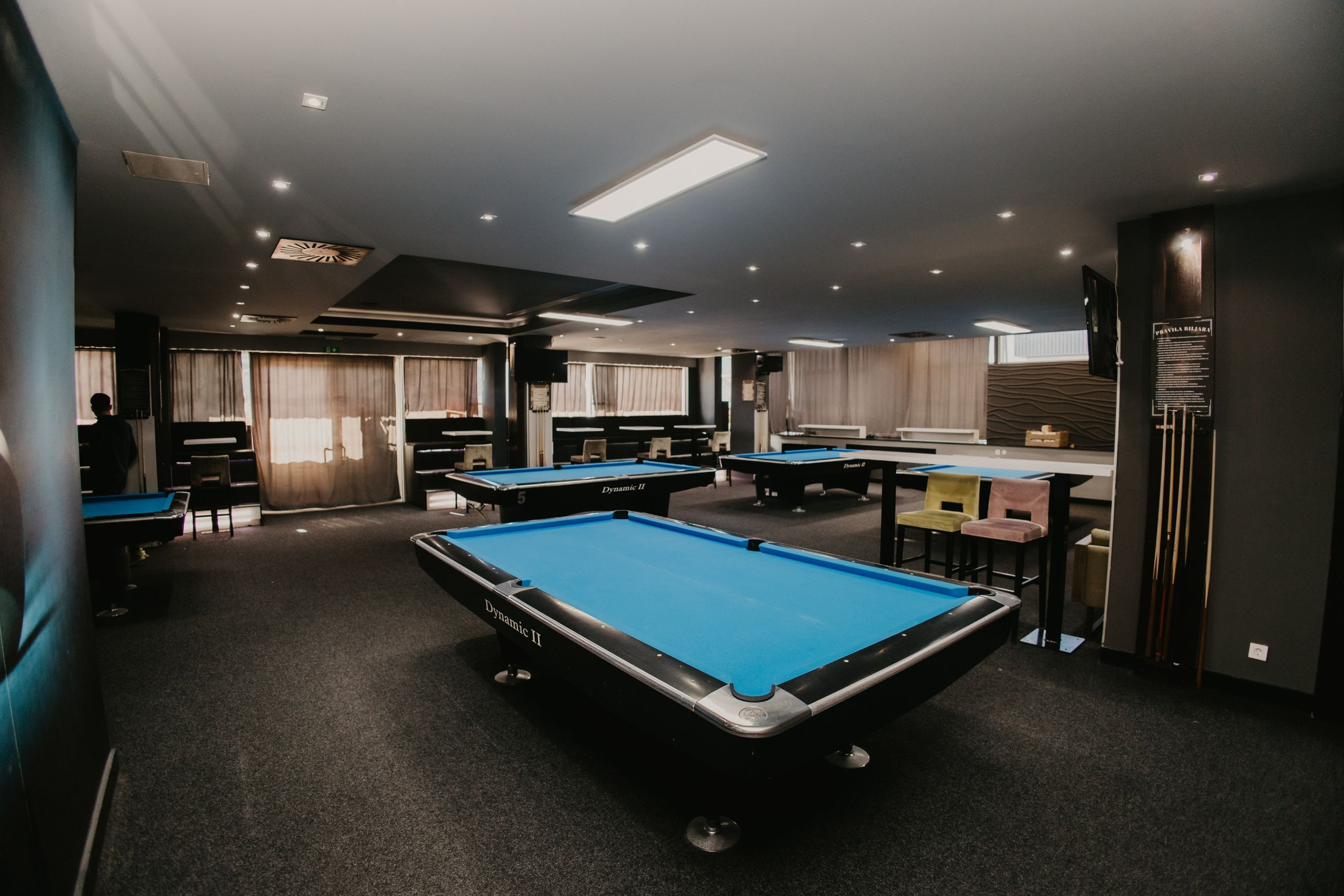 Modern billiards room with multiple pool tables and dark interior design featuring blue felt tables.
